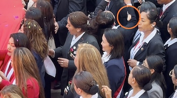 Una multitud vestida con trajes oscuros recibe confeti, mientras un círculo naranja resalta un pequeño objeto blanco en el aire