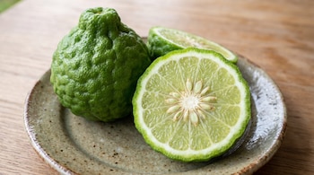 Una bergamota verde rugosa entera y una rodaja cortada con semillas sobre un plato de cerámica en una mesa.