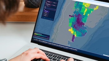 Manos de una persona sobre el teclado de una computadora portátil que muestra un mapa con datos agronómicos en pantalla