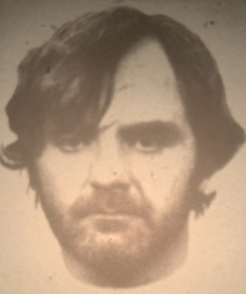 Primer plano de un hombre con pelo oscuro y barba, mirando al frente. La imagen tiene un tono sepia o monocromático, con aspecto envejecido