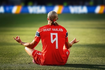 Vista trasera de un futbolista rubio sentado en el césped, con camiseta roja número 9 "BRAUT HAALAND", en postura de meditación