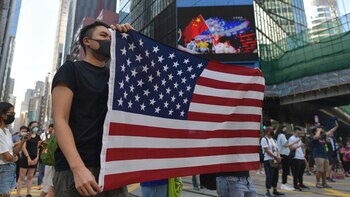 La gente muestra una bandera de Estados Unidos mientras participa en una protesta contra la prohibición del gobierno de que los manifestantes lleven máscaras faciales (Foto de Nicolas ASFOURI / AFP)
