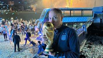 Mickey Singh besa un trofeo dorado con una base verde, vestido con un chándal oscuro, en un autobús descapotable bajo fuegos artificiales y confeti azul y blanco