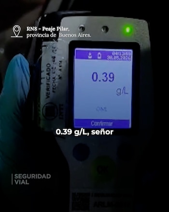 Un alcoholímetro digital muestra la lectura de 0.39 g/L. Una mano enguantada de azul sostiene el dispositivo en un entorno oscuro