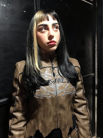 Nicki Nicole muestra su nuevo corte de cabello con flequillo recto y melena oscura mientras posa con los ojos entrecerrados y los labios pintados de rojo.