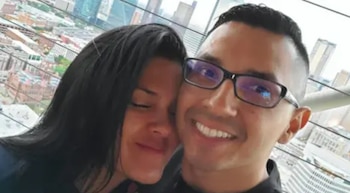 Primer plano de una pareja joven sonriendo. Un hombre con gafas y una mujer con cabello oscuro posan contra un fondo urbano borroso