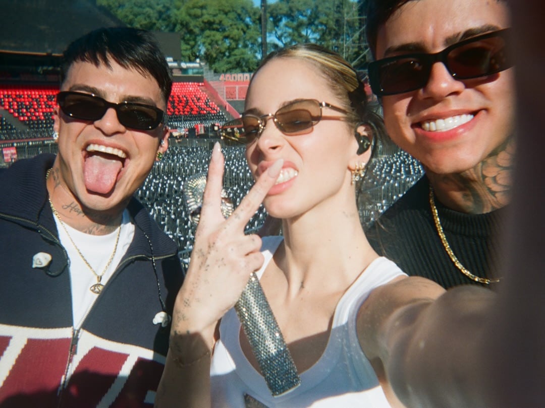 La cantante Tini Stoessel se toma una selfie sonriente con dos amigos en medio de su vibrante concierto en Rosario, con el público de fondo.