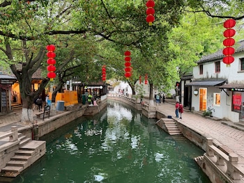 Canal flanqueado por paseos de piedra con escalones, árboles con faroles rojos colgantes, edificios bajos y peatones