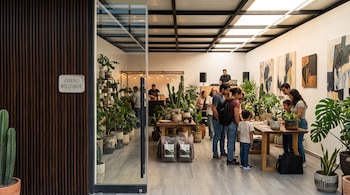 Varias personas observan plantas y macetas en un salón con cuadros en las paredes y un letrero que dice Vivero Boutique.