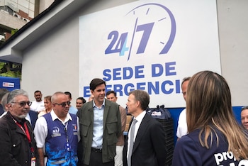 Un grupo de personas conversa frente a un letrero con la frase 24/7 SEDE DE EMERGENCIA y varias cajas apiladas al fondo