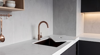 Fregadero de cocina con grifo de cobre, encimera de mármol blanco, estante de madera, cuencos de cerámica y utensilio de cobre.