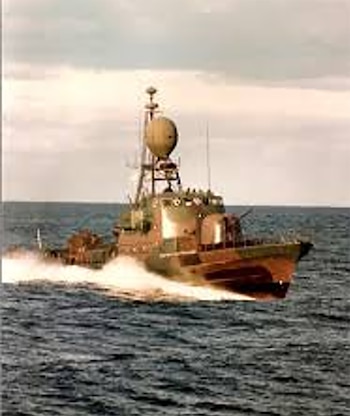 Vista lateral de un barco de patrulla militar camuflado navegando a gran velocidad sobre el agua oscura, generando una estela de espuma blanca