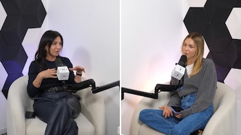 Dos mujeres sentadas en sillones blancos frente a micrófonos en un estudio con paredes de paneles hexagonales negros y blancos