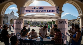 Personas firman documentos en un puesto con toldo y pancartas de Poder Ciudadano, que dice '4 de Julio: Reforma Judicial'. Al fondo, un volcán.