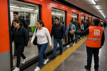 Varias personas salen de un tren naranja en un andén mientras un empleado con chaleco de seguridad les señala la dirección.
