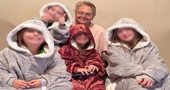 Una mujer mayor con gafas sonríe. Cuatro niños con rostros borrosos llevan sudaderas con capucha tipo manta; tres son grises y una es roja