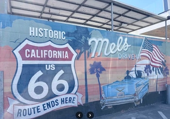 Mural pintado con el escudo de la Ruta 66, un automóvil clásico azul, la bandera de Estados Unidos y la frase Mel's Drive-In