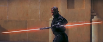 Un personaje de piel roja y negra con cuernos, vistiendo túnica negra, empuña un lightsaber doble de hojas rojas. De fondo, una pared clara