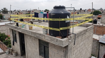 Un tinaco negro de agua y ropa puesta a secar en una azotea cercada con cinta amarilla de precaución.