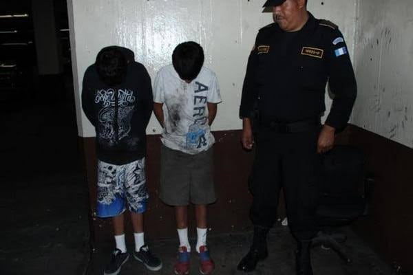 Un agente de la Policía Nacional Civil custodia a dos jóvenes retenidos contra una pared en la Zona 6. (PNCdeGuatemala)