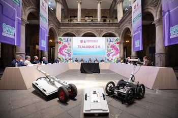 Funcionarios del Gobierno de la CDMX en una sala histórica presentando el plan 'Tlalocque 2.0'. En primer plano, dos robots de inspección de drenaje. Fondo: pantalla y banners institucionales