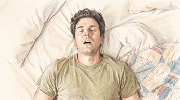Hombre adulto blanco durmiendo boca arriba en una cama, con los ojos cerrados y la boca abierta. Viste una camiseta verde oliva y está cubierto por una manta de retazos. Ilustración.
