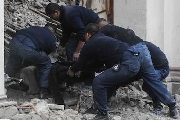 Cuatro hombres se inclinan sobre escombros y restos de una estructura colapsada. Un hombre lleva un distintivo en el bolsillo del pantalón
