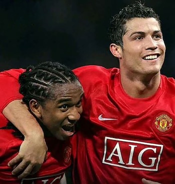 Dos futbolistas, Cristiano Ronaldo y Anderson Luis de Aberu Oliveira, en camisetas rojas del Manchester United, se abrazan sonriendo en el campo