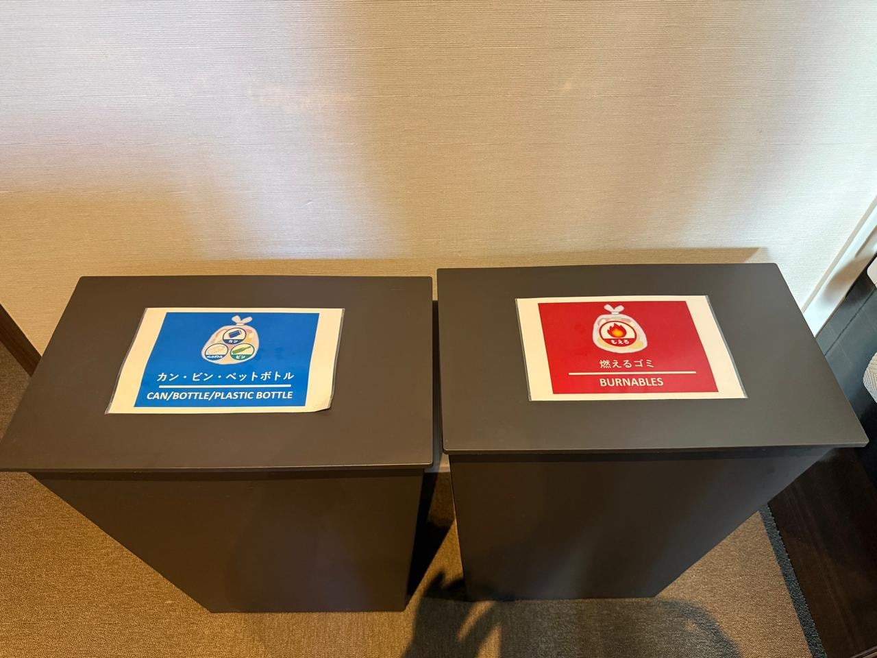 Dos contenedores de basura en Japón muestran la separación de residuos con etiquetas para latas, botellas, plásticos y materiales incinerables. (Infobae)
