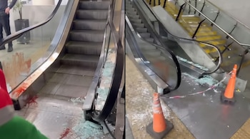 Dos vistas de una escalera mecánica con paneles de vidrio fracturados, restos en el suelo, manchas rojas y conos de tráfico.