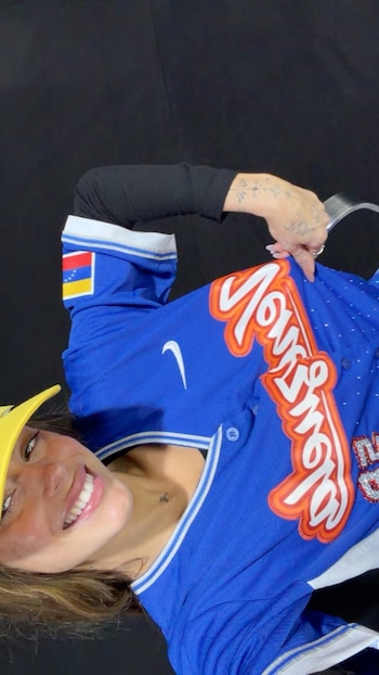 Una mujer sonriente con visera amarilla viste una camiseta azul con la palabra Venezuela en el pecho y una bandera en la manga