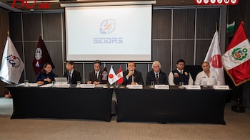 Siete personas sentadas en una mesa con micrófonos, vasos, banderas de Perú, Japón, JICA y UNI. Un proyector muestra el logo SEIDAS