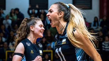 Dos jugadoras de voleibol vestidas con camiseta negra celebran un punto frente a la tribuna de espectadores al fondo