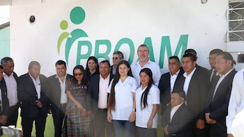 Grupo de personas, incluyendo funcionarios y personal de salud, posa frente a una pared blanca con el logotipo verde de PROAM en Chimaltenango