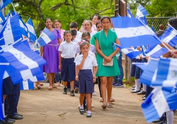 Estudiantes y padres de familia de la zona de los exbolsones ingresan al punto de encuentro en Pasamono entre vallas de honor y banderas salvadoreñas (Cortesía Secretaría de Prensa).