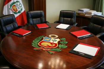 Mesa ovalada de madera oscura con el escudo de Perú y cinco sillas de cuero negro. Carpetas rojas y blancas con plumas. Bandera peruana y documentos al fondo.