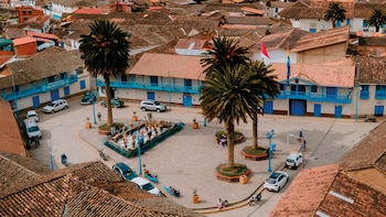 Vista desde lo alto de una plaza urbana rodeada por casas con tejados de arcilla, balcones azules, palmeras y vehículos estacionados