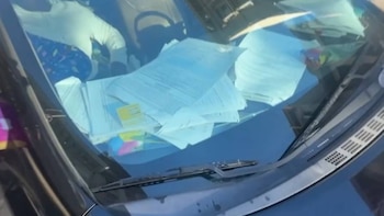 Vista aérea del interior de un coche, mostrando una pila de documentos y papeles sobre el salpicadero. Se ven los limpiaparabrisas y parte de un asiento