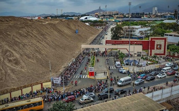 Vista aérea de la entrada a la Universidad Nacional Mayor de San Marcos con personas en fila, vehículos en la calle y un montículo de tierra