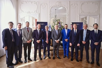 Diez hombres en traje posan en fila dentro de un salón formal con carteles de la Embajada de Argentina en Francia