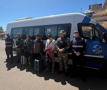 Tres personas con rostros difuminados y maletas están alineadas frente a un vehículo de la Prefectura Naval Argentina junto a cuatro agentes