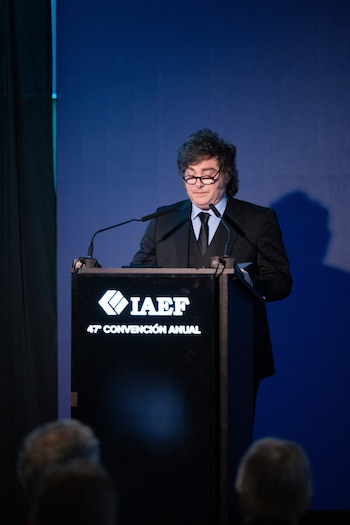 Javier Milei viste traje oscuro y anteojos mientras habla frente a un atril con el logotipo de IAEF sobre fondo azul
