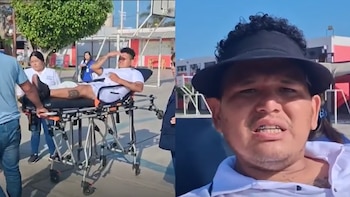 Un hombre con pierna fracturada en camilla es transportado al aire libre. Se ve su rostro en primer plano con visera. Hay personal de apoyo y edificios al fondo