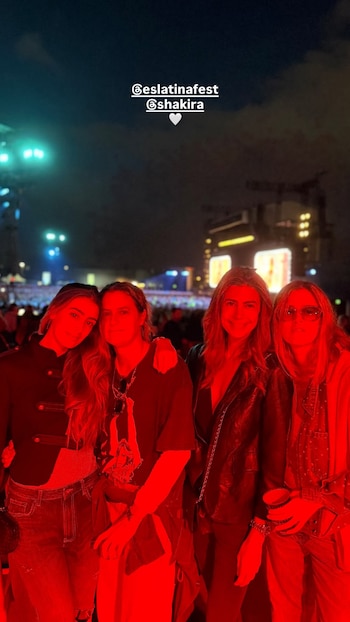 Cuatro mujeres posan bajo una luz roja en un recinto al aire libre con un escenario iluminado de fondo