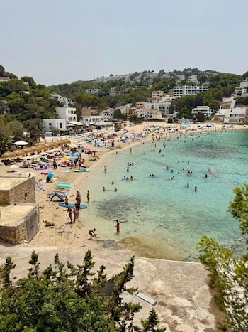 Vista aérea de playa de arena clara, mar turquesa con bañistas, sombrillas y reposeras. Edificios blancos sobre un monte con vegetación