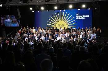 Múltiples personas sentadas en un escenario frente a una pantalla azul con el Sol de Mayo y el texto "el peronismo debate". Audiencia en primer plano oscuro
