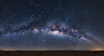 Ilustración nocturna de la Vía Láctea vista desde un desierto, con varios agujeros negros representados a lo largo de la banda central de la galaxia bajo un cielo estrellado.