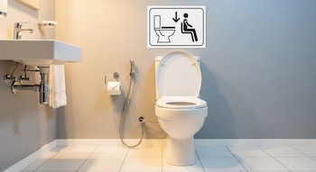 Baño moderno con inodoro blanco, lavabo blanco, toalla, papel higiénico, bidet y señal que muestra a una persona sentada en el inodoro.