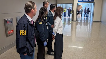 Varios agentes con la sigla FBI en sus chaquetas sujetan a una mujer esposada en el pasillo de un aeropuerto