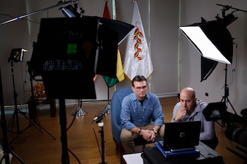 Dos hombres observan una computadora portátil rodeados de equipos de iluminación y con banderas al fondo